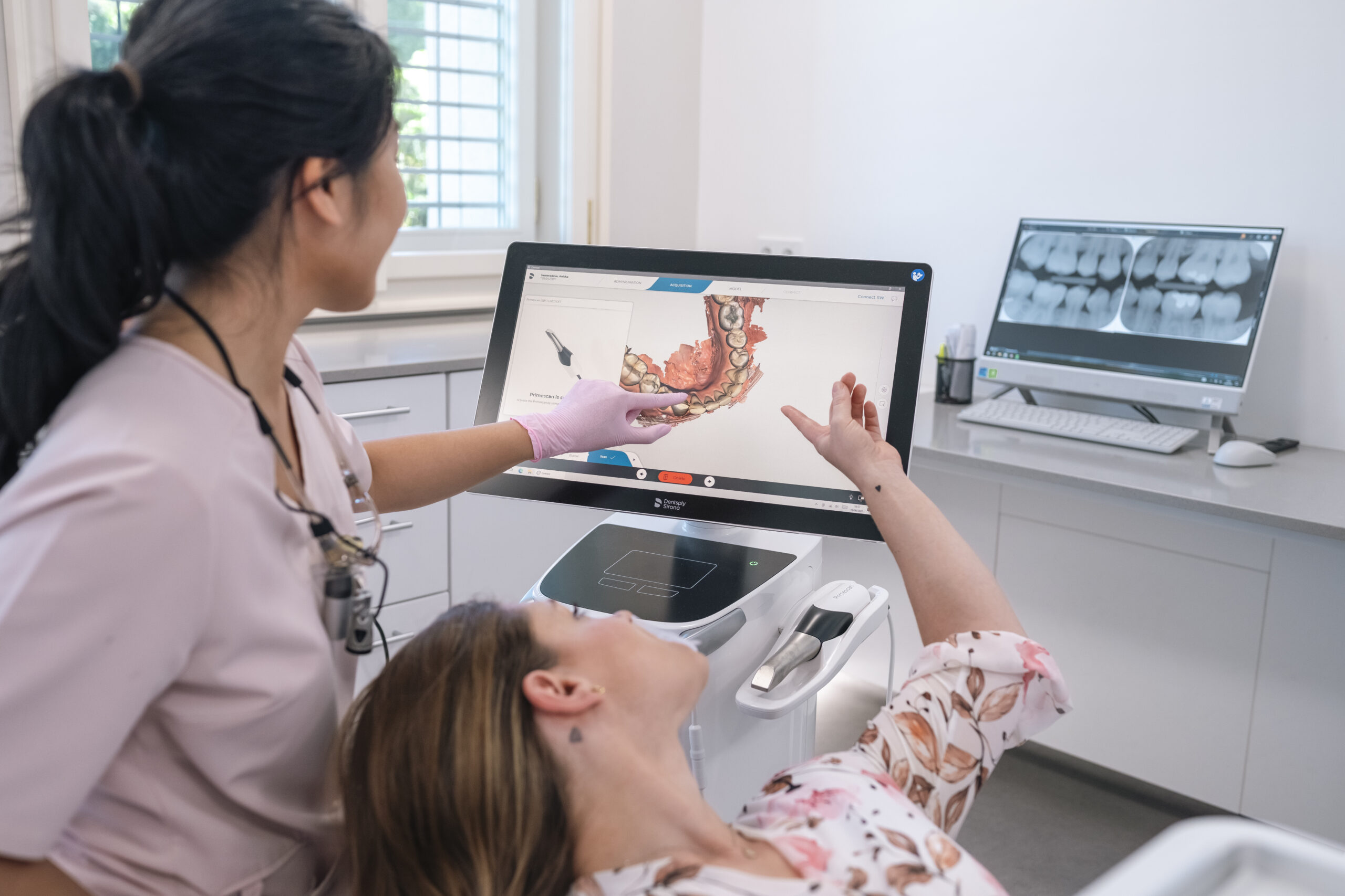 Zubní lékařka vysvětluje pacientce 3D sken chrupu na monitoru